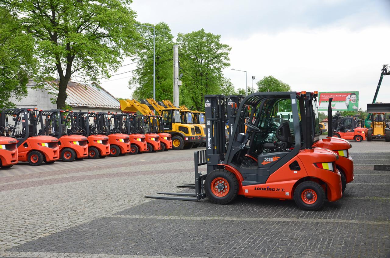 Rząd pomarańczowych wózków widłowych marki Lonking ustawionych na brukowanym placu, z żółtymi koparkami w tle i reklamą na billboardzie w oddali.