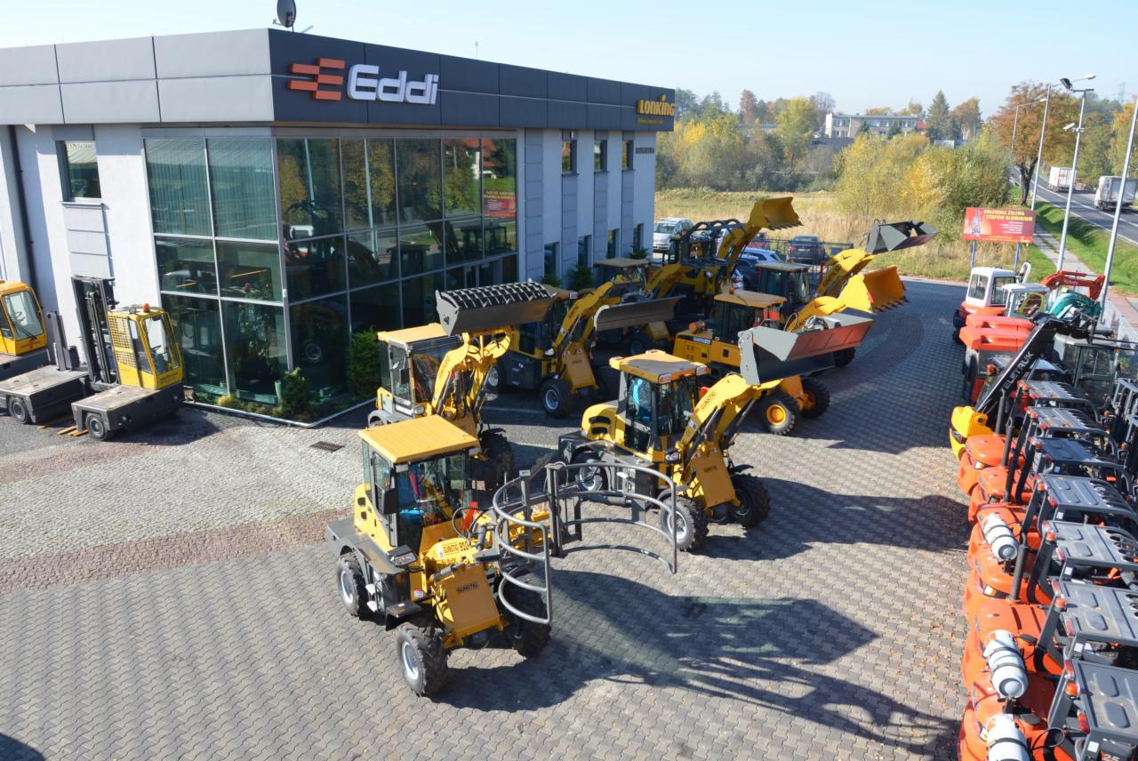 Plac z nowymi maszynami budowlanymi i wózkami widłowymi przed budynkiem firmy Eddi Lonking, widoczne różne modele i typy maszyn w kolorze żółtym i pomarańczowym.
