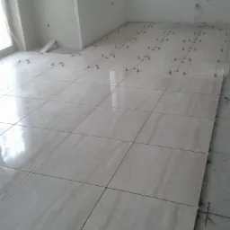 Jasne, kwadratowe płytki podłogowe, ułożone z użyciem systemu poziomowania, w nowym pomieszczeniu z oknem. Widok z góry, na etapie prac wykończeniowych.