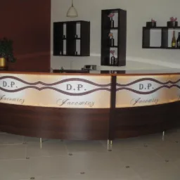 Recepcja z podświetlanym frontem, ciemne drewno i napisy 'D.P. Jacewicz', w tle półki z dekoracjami. Całość w stonowanej kolorystyce.