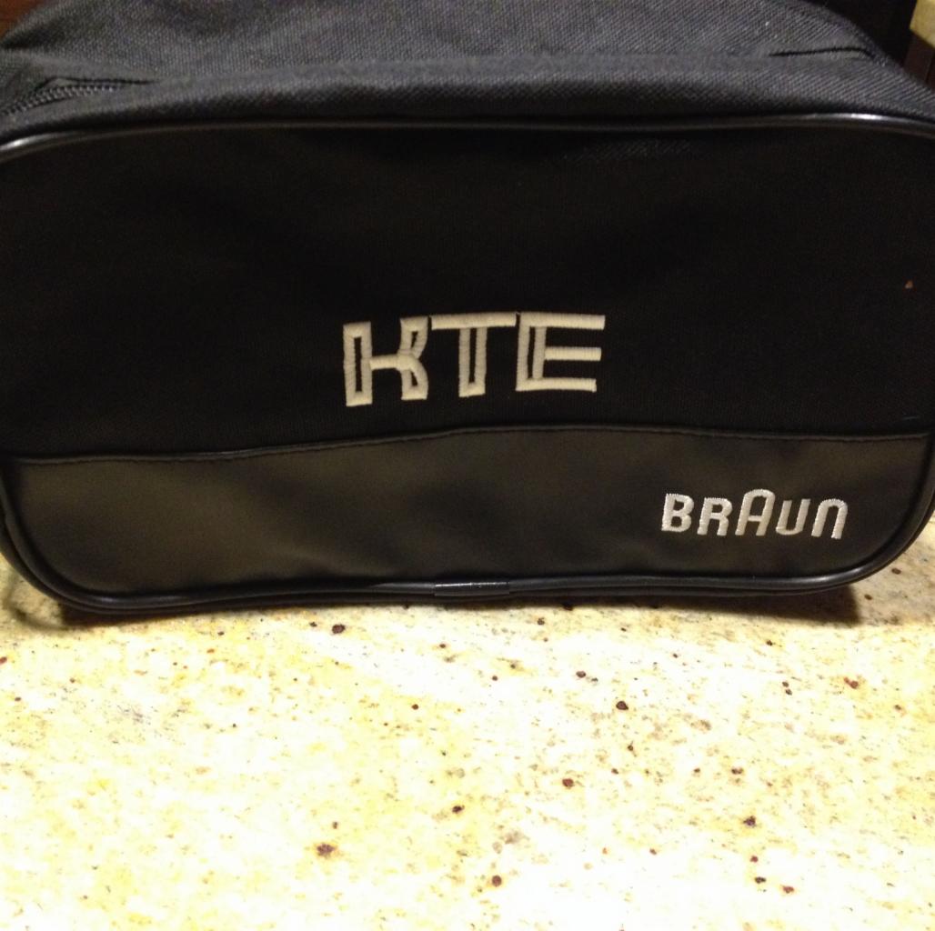 Czarna kosmetyczka z haftowanymi napisami 'KTE' i 'BRAUN' na tle beżowego blatu.