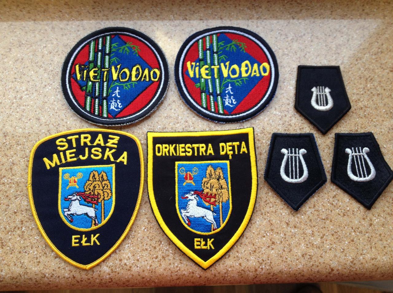 Zestaw naszywek z Ełku: okrągłe naszywki Viet Vo Dao, naszywka Straży Miejskiej, naszywka Orkiestry Dętej oraz naramienniki z lirą.