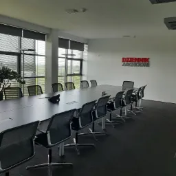 Sala konferencyjna z długim stołem i krzesłami biurowymi, widoczne logo 'Dziennik Zachodni' na ścianie, rolety w oknach i rośliny doniczkowe.