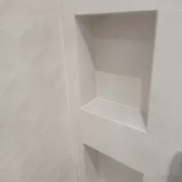 Wykończona wnęka w ścianie wyłożonej jasnymi, matowymi płytkami ceramicznymi, widok z boku, ukazujący detale fug i teksturę płytek.