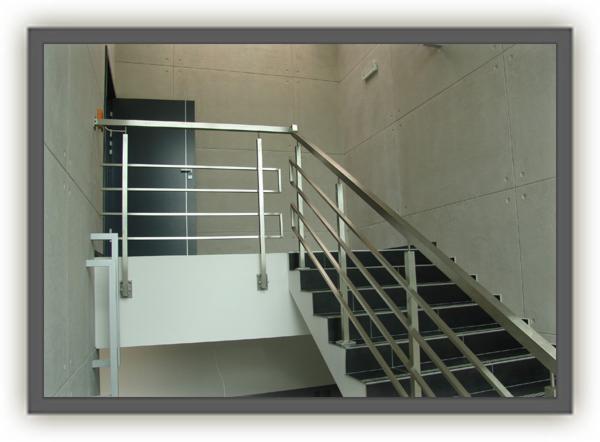 Schody wyłożone czarnymi płytkami z prostą balustradą ze stali nierdzewnej w nowoczesnym wnętrzu.