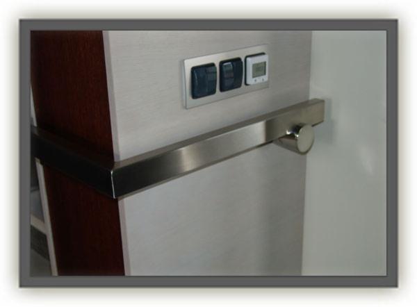 Kwadratowa poręcz ze stali nierdzewnej zamontowana na ścianie obok panelu sterowania oświetleniem i wyświetlaczem temperatury.