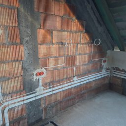 Lumen Tomasz Dobrzyński - Instalacja elektryczna w surowym wnętrzu: kable w białych listwach mocowane do ceglanej ściany, widoczne puszki instalacyjne. Etap prac przed wykończeniem.