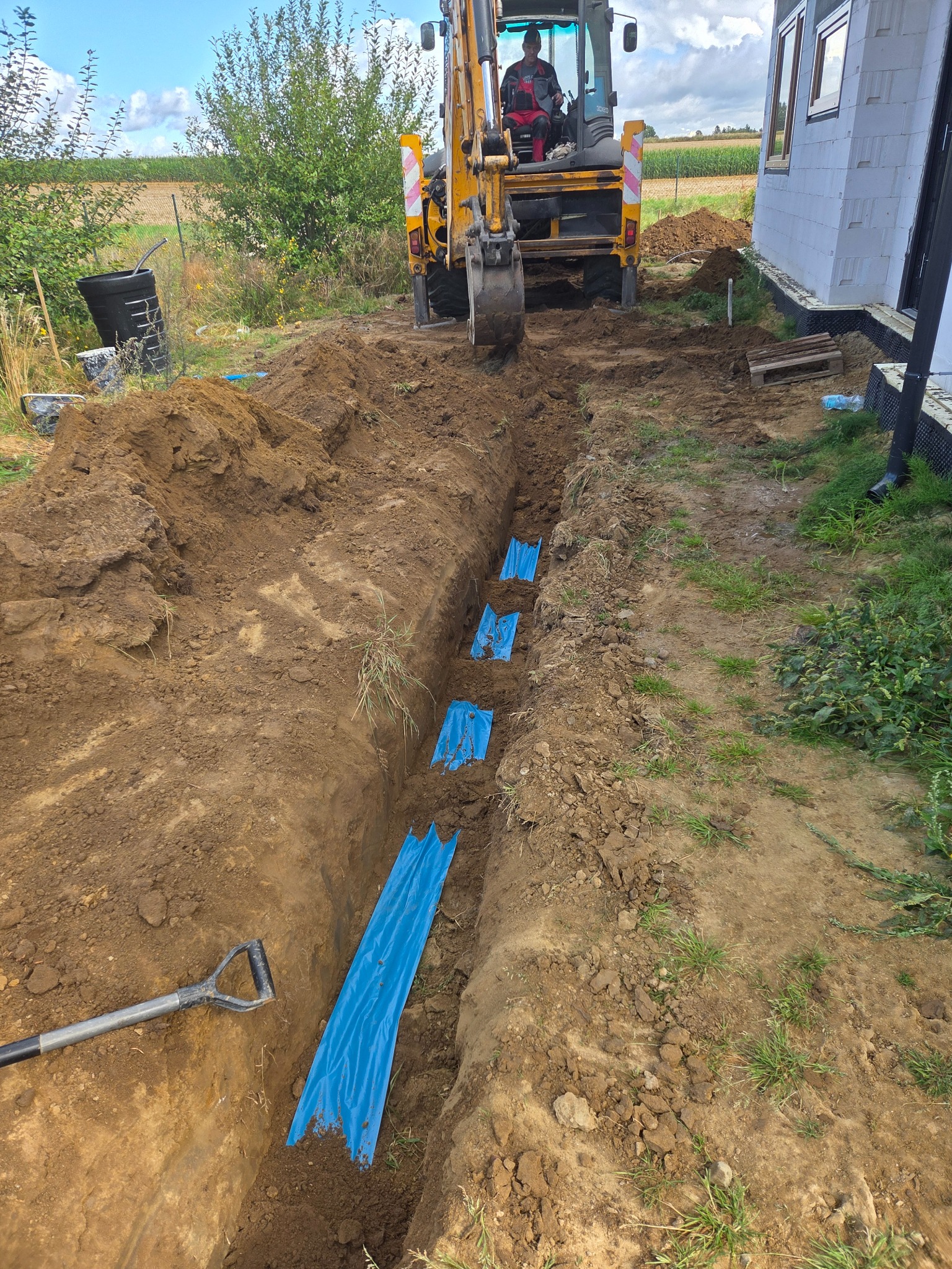 Wykopany rów pod instalację elektryczną z niebieskimi osłonami kabli, koparka w tle, teren budowy. Widok z góry na wykop.