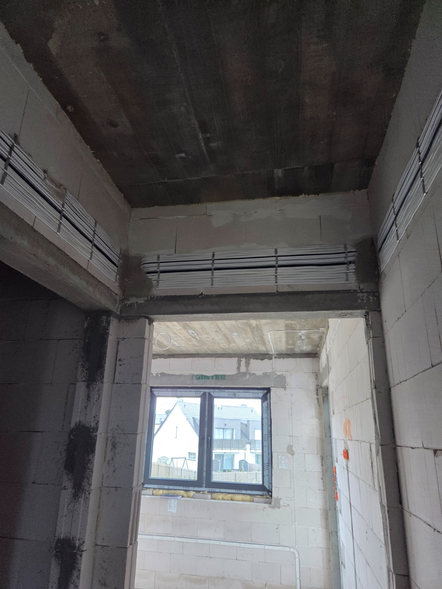 Surowy stan: instalacja kabli w korytkach na ścianach i suficie budynku w trakcie budowy. Widok na okno i dalsze pomieszczenia.