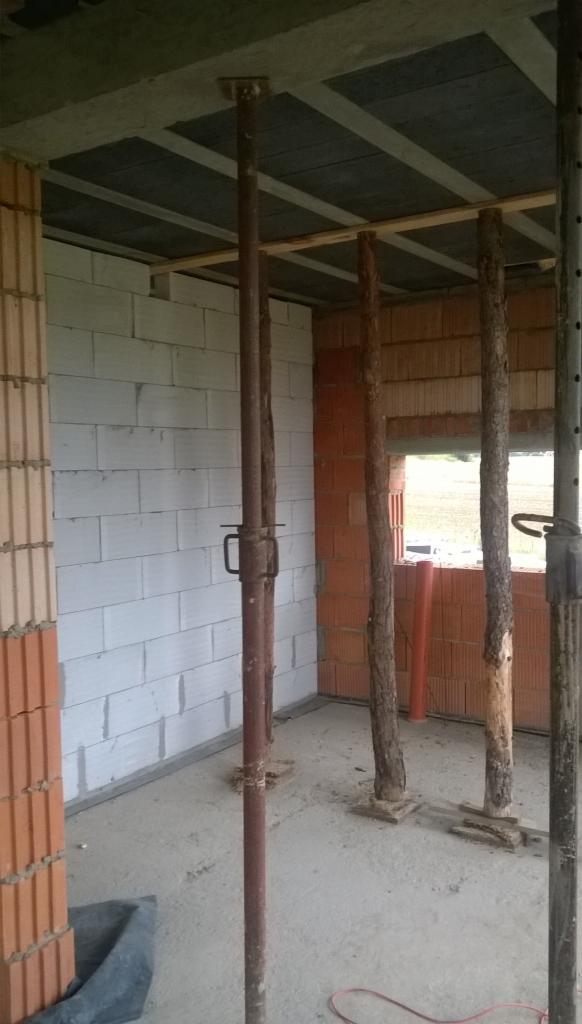 Wnętrze surowego budynku w trakcie budowy, widoczne białe bloczki i cegły, metalowe stemple podtrzymujące strop oraz drewniane podpory imitujące pnie drzew