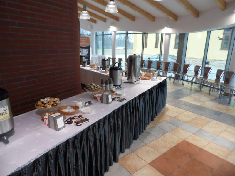 Stół cateringowy z przekąskami, kawą i herbatą w sali konferencyjnej z rzędem krzeseł przy oknie.