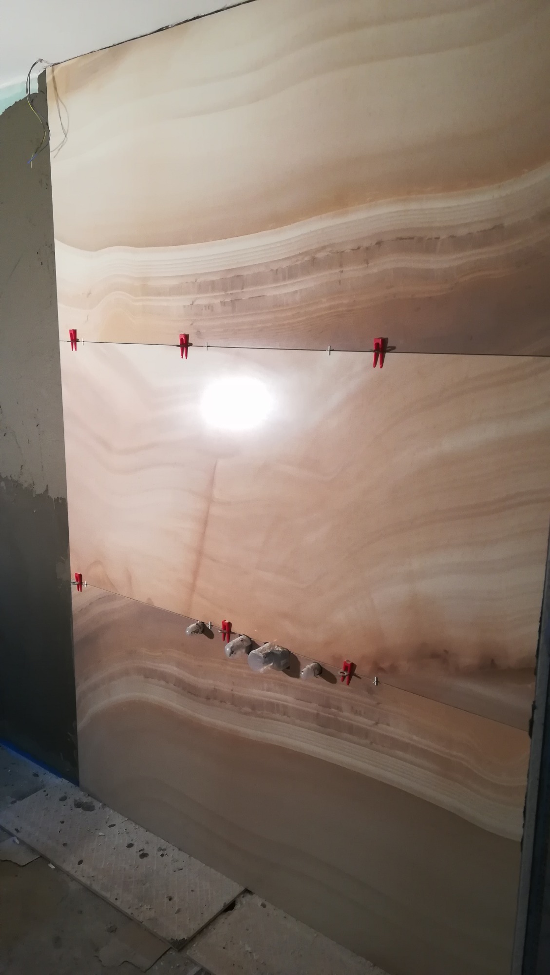 Układanie wielkoformatowych płytek imitujących onyks na ścianie, z użyciem poziomicy, krzyżyków dystansowych i zaprawy klejowej.