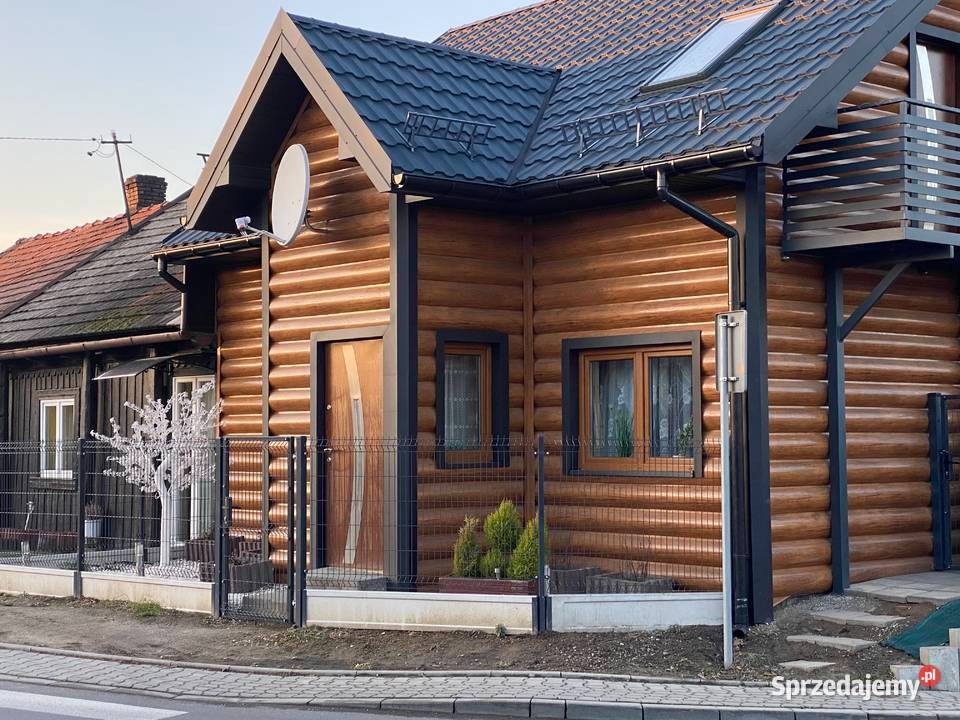 Dom z drewnianą elewacją imitującą bale, czarnym dachem z blachy i rynnami w kolorze grafitowym, widok z zewnątrz na fragment elewacji i dachu.