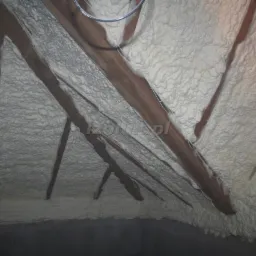 Poddasze z drewnianą konstrukcją krokwiową, ocieplone grubą warstwą natryskowej pianki PUR, widok z dołu, oświetlenie naturalne.