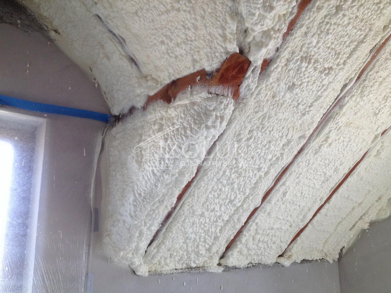 Poddasze po ociepleniu pianką PUR, widoczne krokwie częściowo zakryte pianą. Okno zabezpieczone folią. Wykończona izolacja w narożniku.