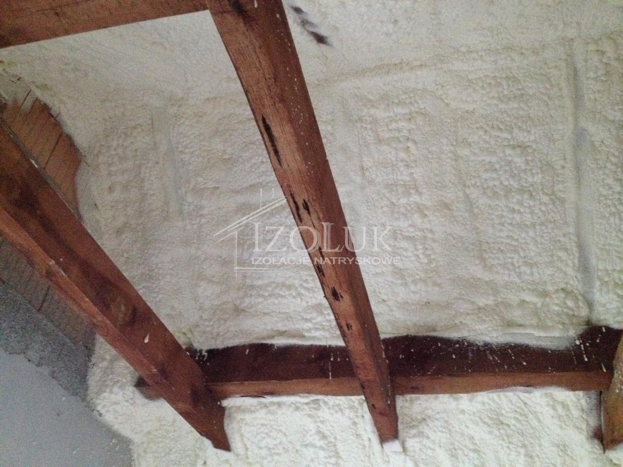 Poddasze ocieplone pianką PUR, widoczne drewniane belki konstrukcyjne i równomierna warstwa izolacji natryskowej. Detal wykończenia izolacji.