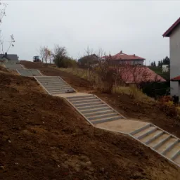 Schody z kostki brukowej prowadzące pod górę, widoczny traktor na szczycie w tle.