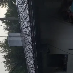 Fragment dachu z blachodachówki trapezowej w kolorze ciemnobrązowym, widoczny komin wentylacyjny, antena telewizyjna, słup oświetleniowy i fragment bałaganu na poddaszu.