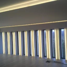 Nowoczesne wnętrze z podświetlanymi pionowymi panelami okiennymi i listwami LED na suficie, widoczne narzędzia na podłodze.