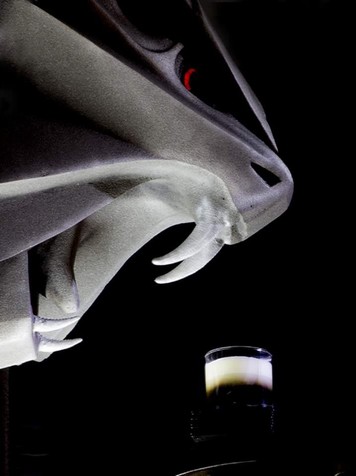 Abstrakcyjna fotografia reklamowa: Szara rzeźba o futurystycznym designie z czerwonym akcentem i szklanka warstwowego napoju na czarnym tle.