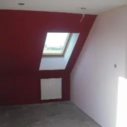 Pokój na poddaszu po malowaniu: ściana bordowa z oknem dachowym, ściana biała, grzejnik. Widoczne ślady po taśmie malarskiej.