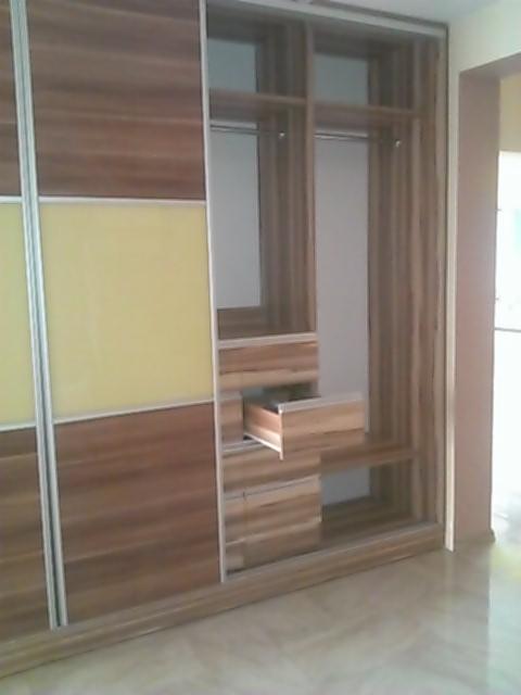 Wnętrze szafy przesuwnej z otwartą szufladą, fronty z okleiną drewnopodobną i żółtym panelem, widoczne półki i drążek na ubrania.