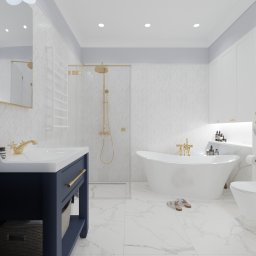 HOME PLAN PROJEKTOWANIE WNĘTRZ JOANNA MIELCZAREK - Elegancka łazienka z białą armaturą, granatową szafką pod umywalką i złotymi detalami, wykończona marmurowymi płytkami w jodełkę.