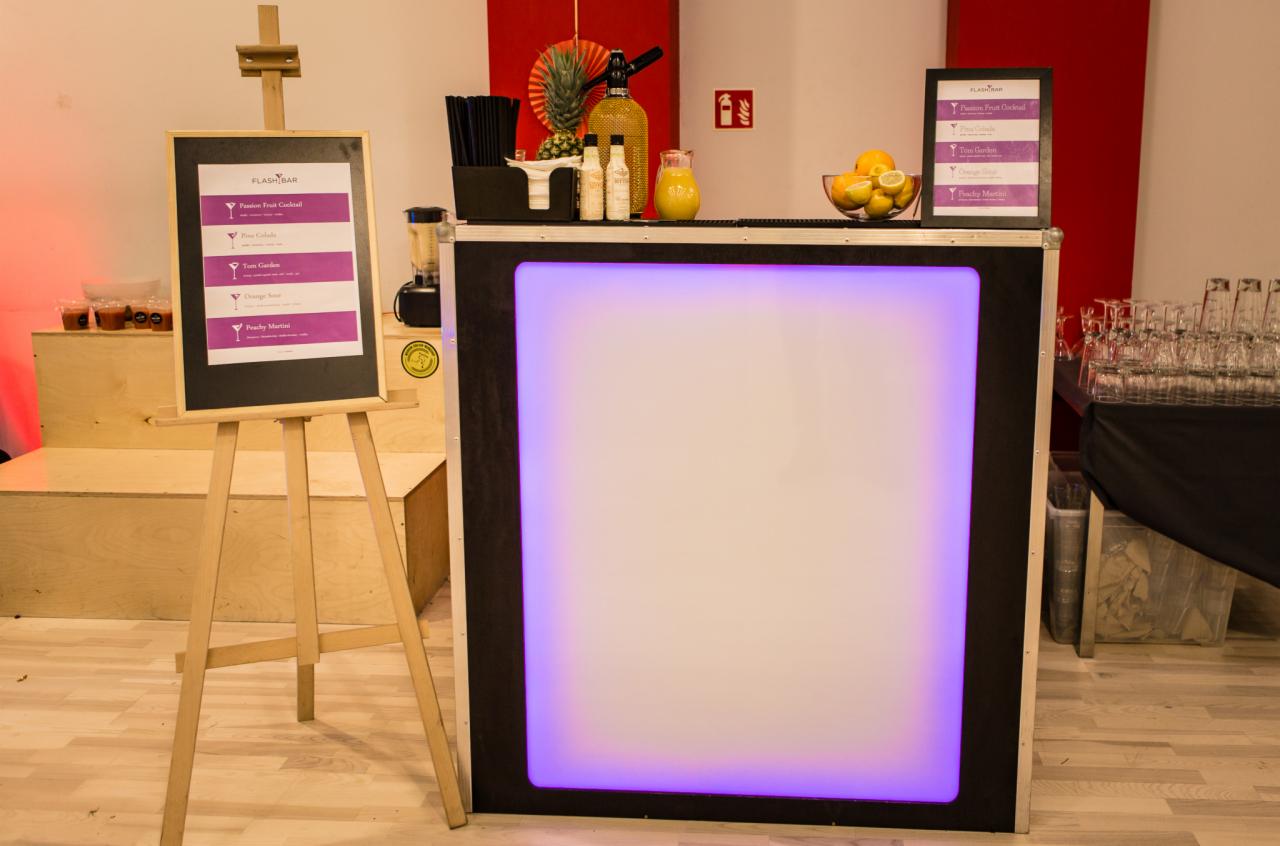 Podświetlany bar z menu drinków na sztaludze, owoce i akcesoria barmańskie w tle, Poznań.