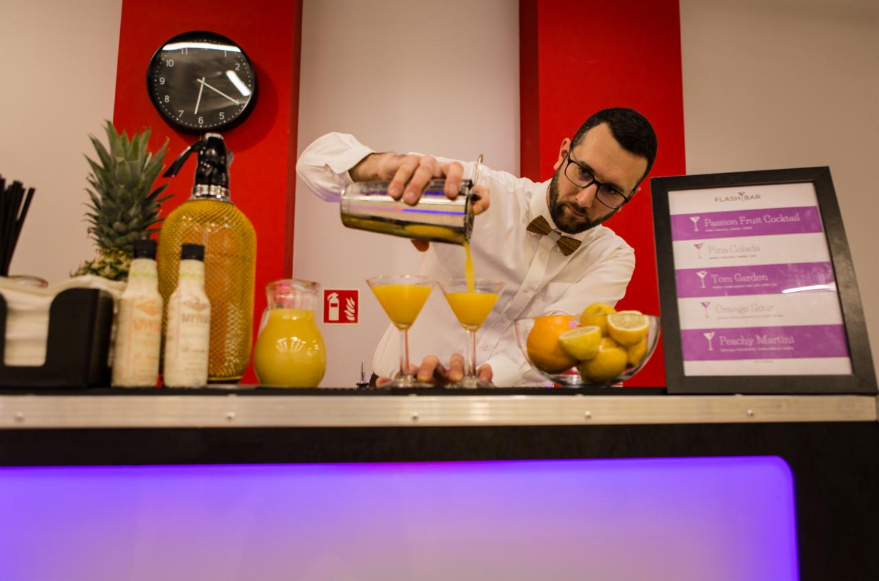 Barmanka w muszce przelewa pomarańczowy koktajl z shakera do dwóch kieliszków martini na barze z owocami i menu drinków.