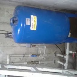 Poziomy, niebieski zbiornik hydroforowy WIMEST ZPL 200/6 z instalacją wodną w piwnicy, widoczne rury PCV i metalowe złączki.