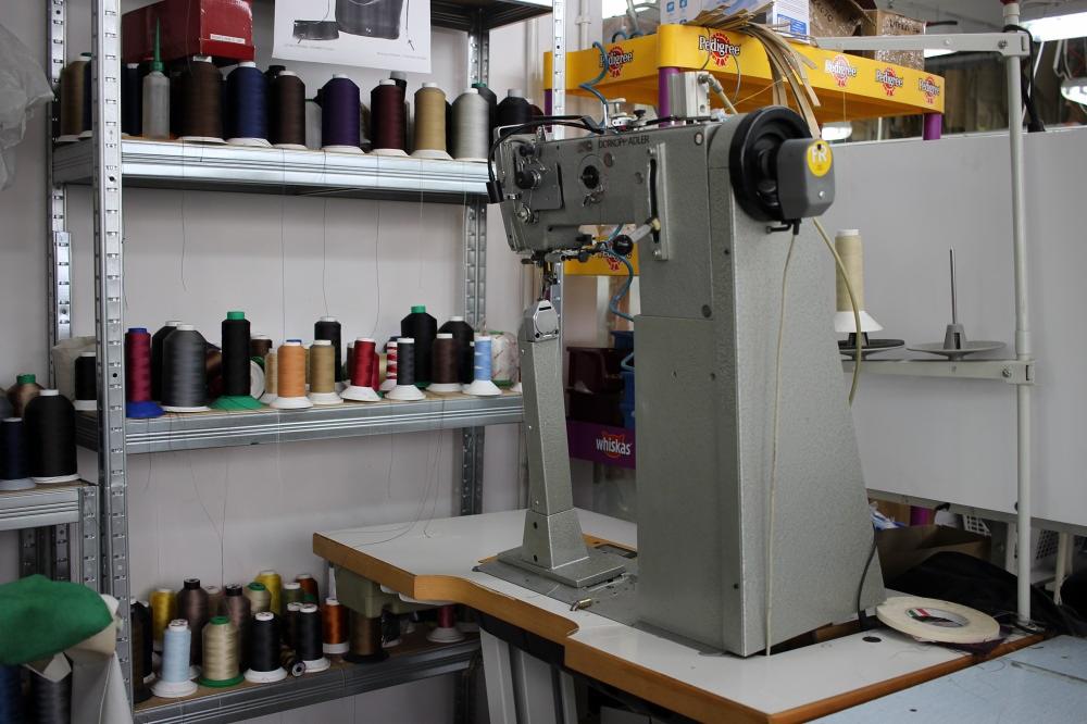 Maszyna szwalnicza marki Dürkopp Adler na stole, z półkami pełnymi nici w tle. Widoczny detal: rolka taśmy dwustronnej obok maszyny.
