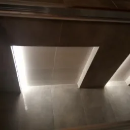 Nowoczesna, szara łazienka z podświetlanymi wnękami w suficie wyłożonymi płytkami ceramicznymi, widok z dołu.