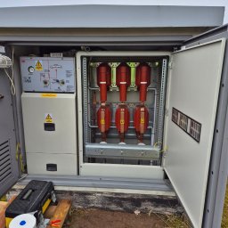 Intek-Tech Technika Instalacji Prażuch Piotr - Otwarta szafa elektryczna z widocznymi zabezpieczeniami i elementami instalacji. Na zewnątrz skrzynka narzędziowa i akcesoria.