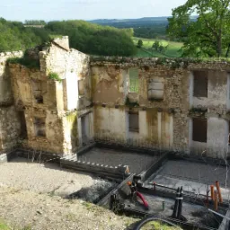 Ruiny kamiennego budynku z odsłoniętymi fundamentami i nową konstrukcją szalunkową, widok na zielone wzgórza w tle.