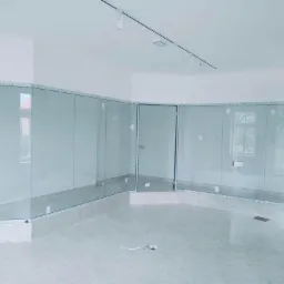 Szklana zabudowa wewnętrzna w jasnym pomieszczeniu, widoczne szklane ścianki działowe z białymi profilami, minimalistyczne oświetlenie sufitowe.