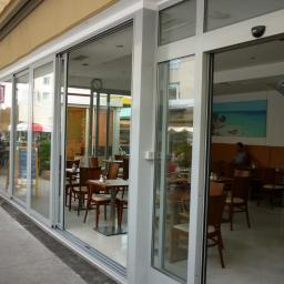 Vobitech Sp. z o.o. - Szerokie, przeszklone drzwi przesuwne z aluminium, oddzielające wnętrze kawiarni od chodnika, widoczne menu na tablicy przed wejściem.