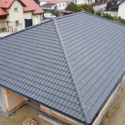 Nowy, grafitowy dach z dachówki ceramicznej na budynku w trakcie budowy, widok z góry, ceglana konstrukcja ścian, otoczenie w stanie surowym.