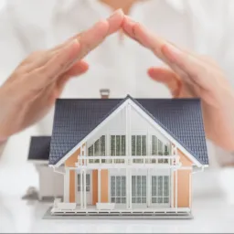 Model domu jednorodzinnego chroniony dłońmi, koncepcja ubezpieczenia nieruchomości.