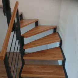 Drewniane schody ze stalową konstrukcją i poręczą, widok od dołu, minimalistyczny design, jasne wnętrze.