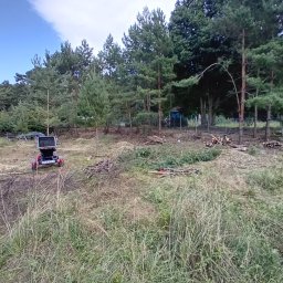 ARKADIAS Arkadiusz Wysocki - Teren po wycince drzew z widoczną rębarką do gałęzi i stertami pociętych gałęzi. W tle drzewa iglaste i fragment budynku.