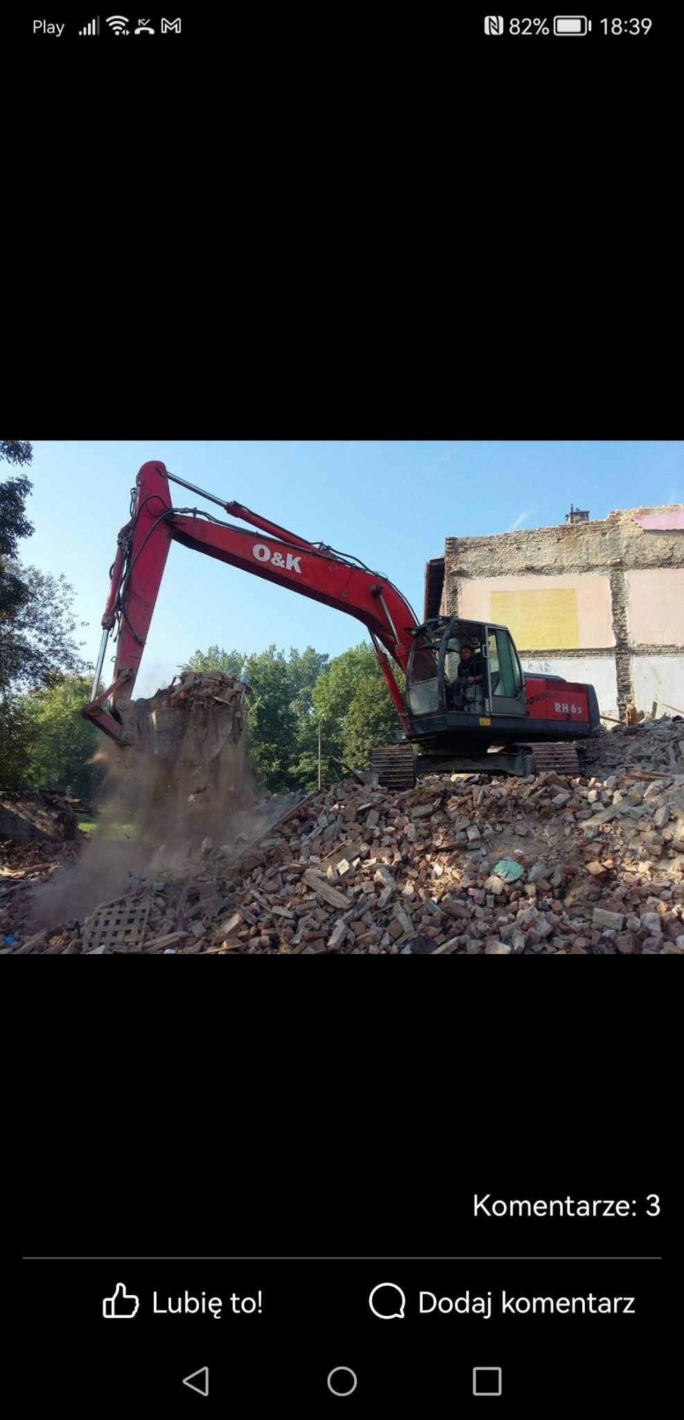 Czerwona koparka O&K RH6s rozbiera gruz budynku, z unoszącym się pyłem i stertą cegieł w tle.