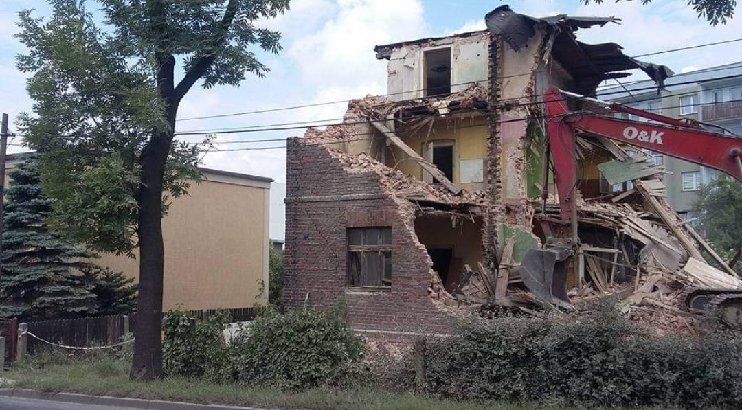 Częściowo zburzony, ceglano-żółty budynek w Bytomiu podczas rozbiórki, z widoczną czerwoną koparką O&K i stertą gruzu.