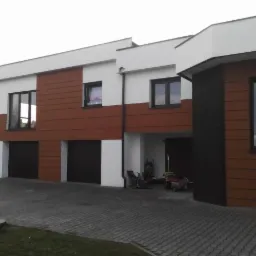 Nowoczesny dom z dwoma garażami, wykończony panelami w odcieniach brązu i czerni, z widocznym podjazdem z kostki i fragmentem zieleni.