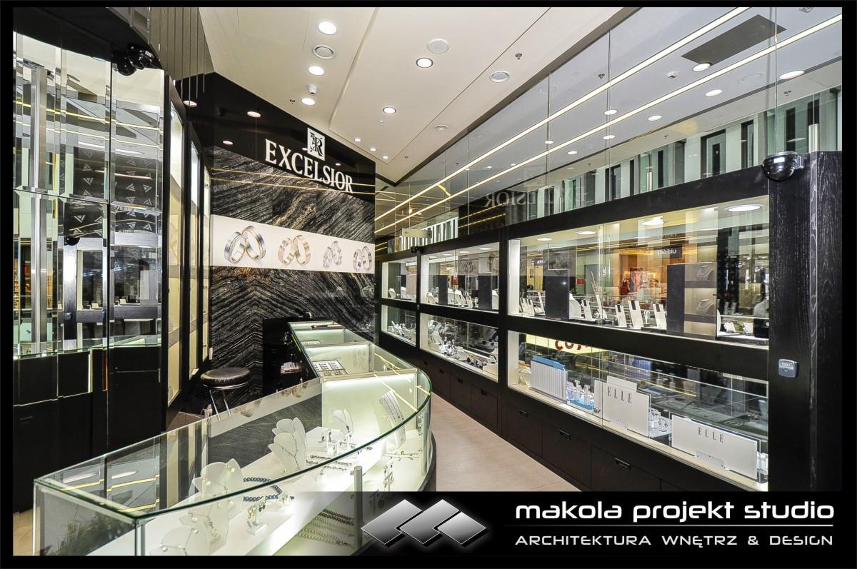 Nowoczesny projekt wnętrza sklepu jubilerskiego z przeszklonymi witrynami i marmurową ścianą z logo 'Excelsior', oświetlony punktowo.