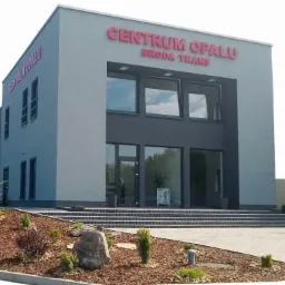 Nowoczesny budynek Centrum Opału Broda Trans z dużymi oknami, schodami wejściowymi i zagospodarowanym terenem zielonym. Jasnoszara elewacja z czerwonym napisem.