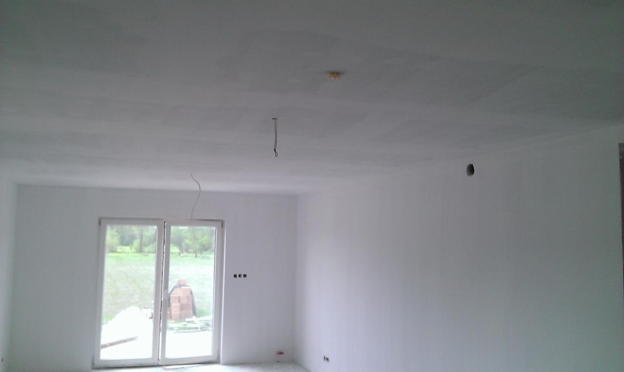 Wnętrze po malowaniu ścian i sufitu na biało, widoczne gładzie. Okno balkonowe z widokiem na zewnątrz. Przygotowane punkty elektryczne.