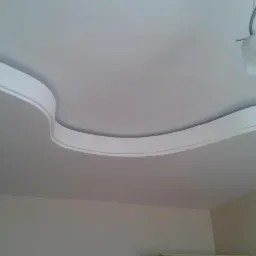 Dekoracyjny sufit podwieszany z falistą listwą ozdobną, oświetlenie punktowe. Estetyczne wykończenie wnętrza z dbałością o detale.