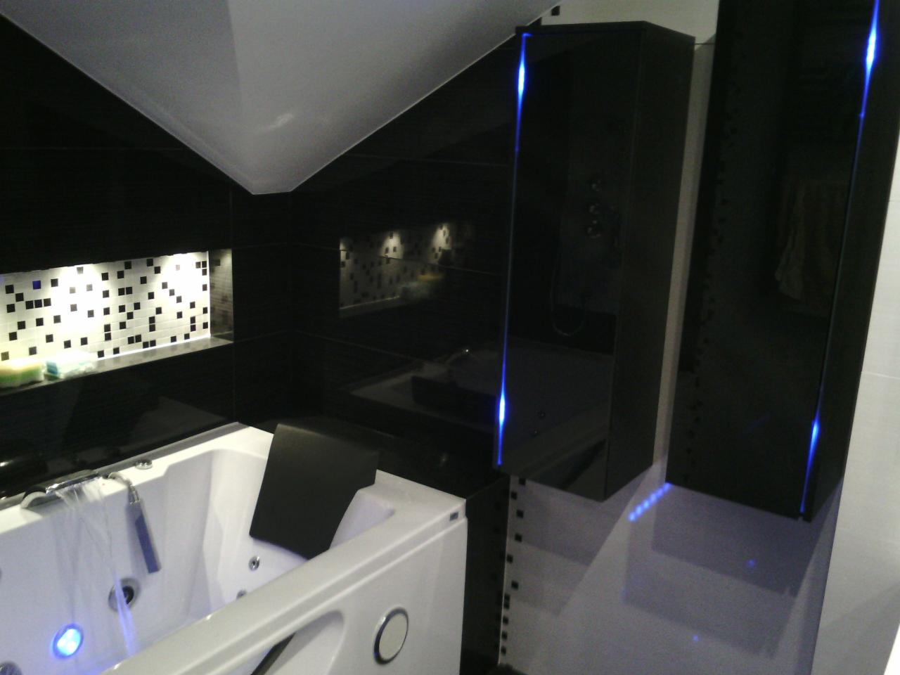 Nowoczesna łazienka z białą wanną z hydromasażem, czarnymi płytkami i szafkami z podświetleniem LED. Widoczne mozaiki i armatura.