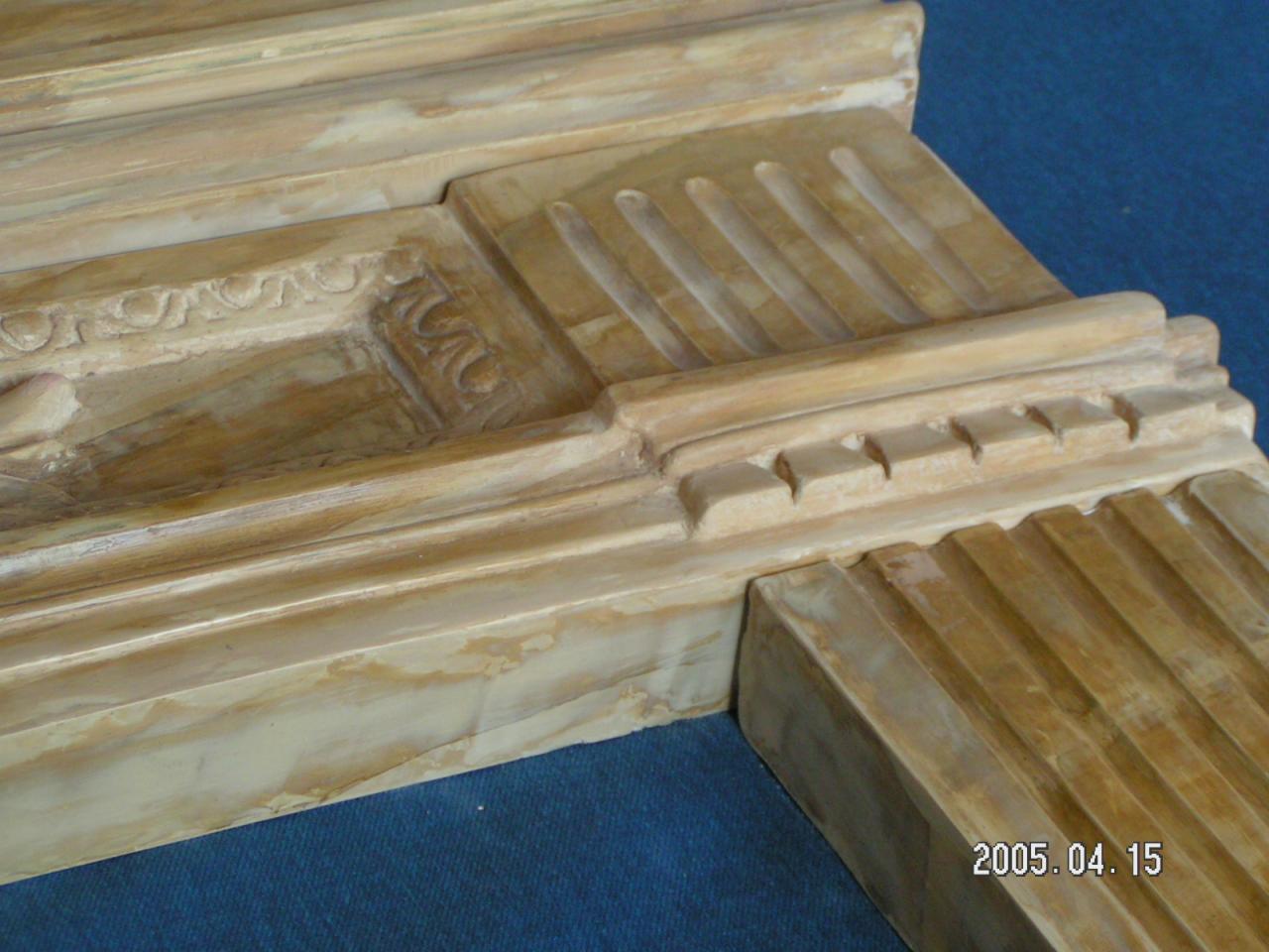 Fragment kominka klasycystycznego z beżowego marmuru, widoczne detale zdobień i data '2005.04.15' w prawym dolnym rogu.