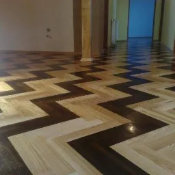 Parkiet ułożony w jodełkę z dwóch odcieni drewna: jasnego i ciemnego, tworzący zygzakowaty wzór na podłodze w korytarzu.